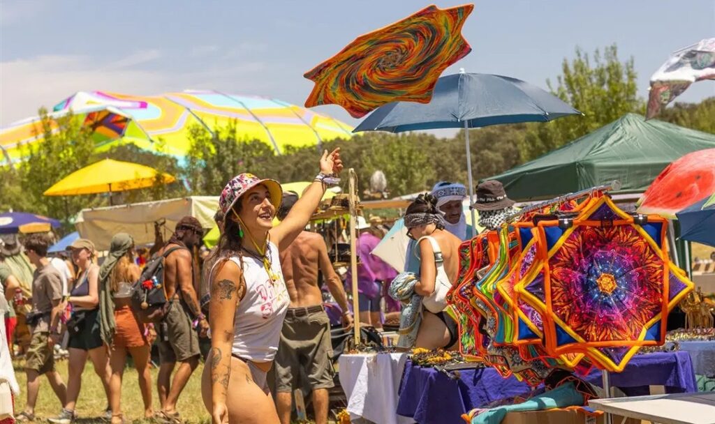 A festivalgoer browsing colorful, psychedelic decorations at an outdoor market stall during Boom Festival