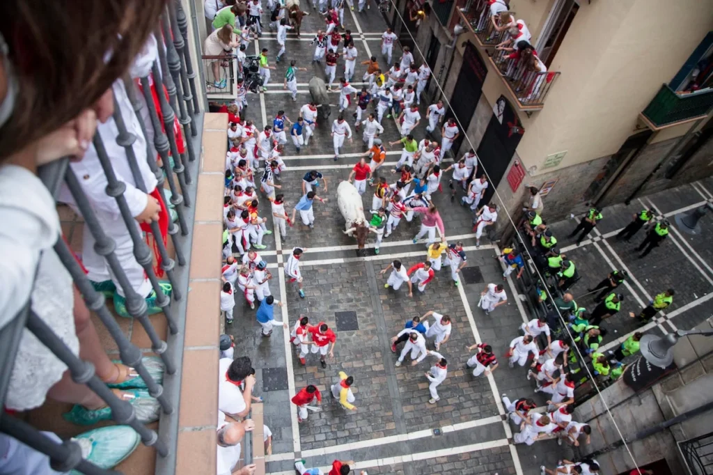 High-angle view of a bull running down a narrow, crowded street during the Running of the Bulls in Pamplona
