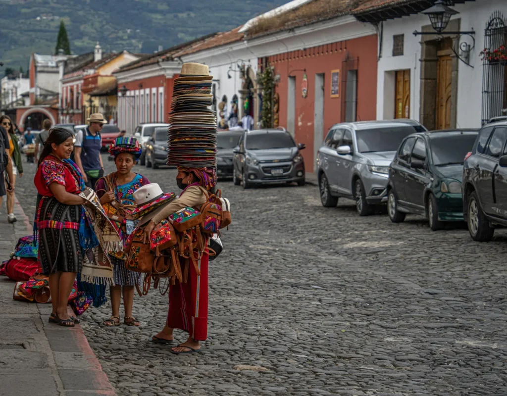 Indigenous women selling textiles and hats on a cobblestone street in Antigua