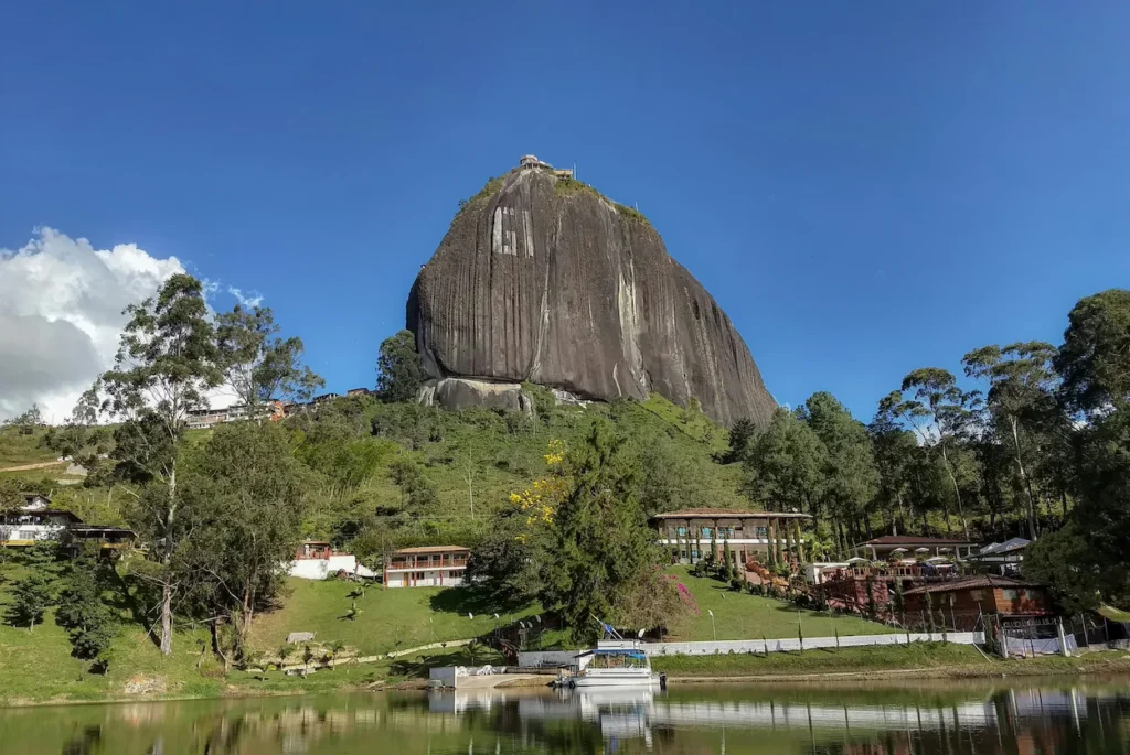 Guatape rock monolith standing tall above a calm lake with green hills and buildings at its base