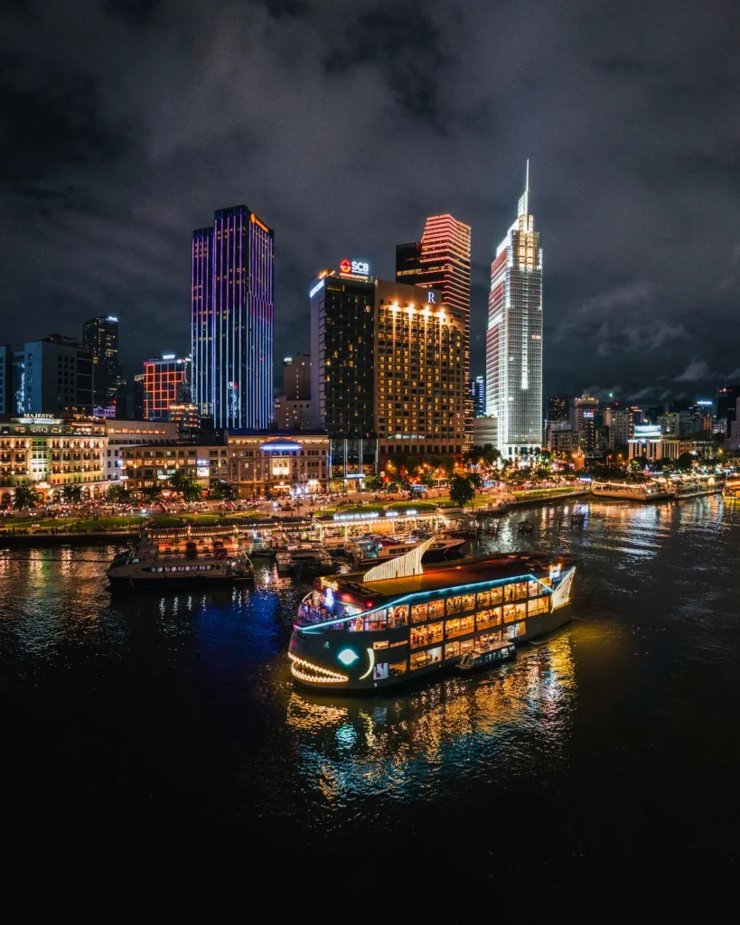 Illuminated cruise boat sailing along the Saigon River in front of the nighttime city skyline