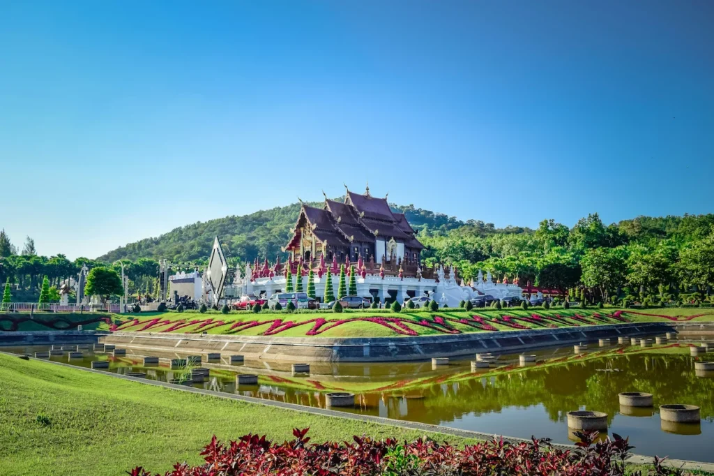 Ho Kham Luang pavilion at Royal Park Rajapruek reflecting on a calm pond under a blue sky