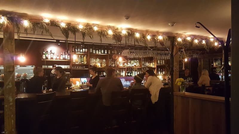 A dimly lit bar at Café Adam with bottles on shelves and patrons seated.