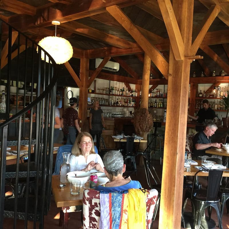 Inside Cantina 229, diners at wooden tables under a vaulted ceiling with exposed beams.