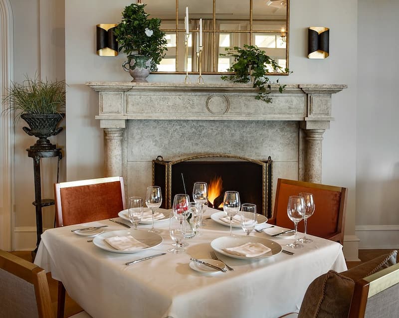 An elegant dining table set for four in front of an ornate stone fireplace.
