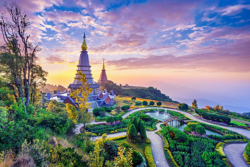 Two grand pagodas amidst landscaped gardens on a mountaintop at sunset in Chiang Mai, Thailand.