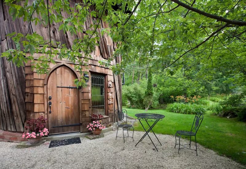 A unique wooden tower with an arched door, set amidst lush green foliage.