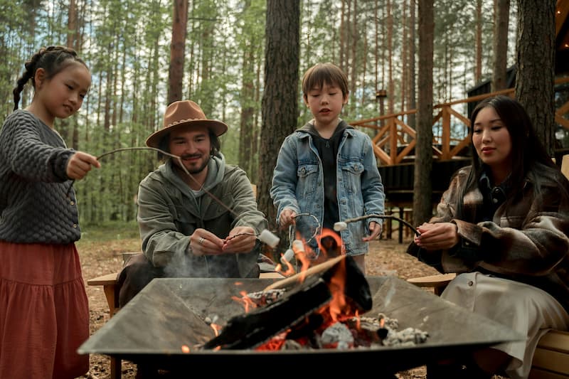 A family roasts marshmallows over a campfire in a forest.