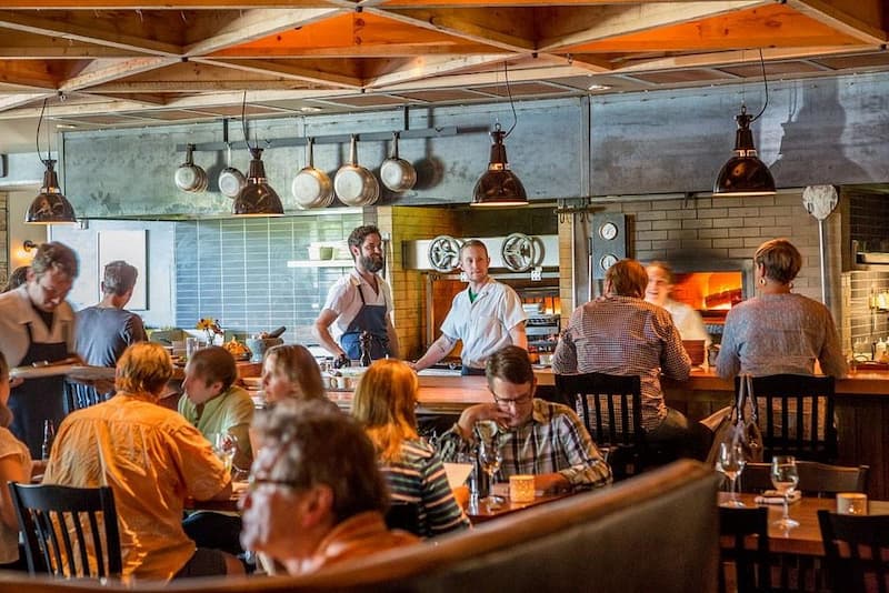 A bustling restaurant with an open kitchen, chefs at work, and a wood-fired oven.