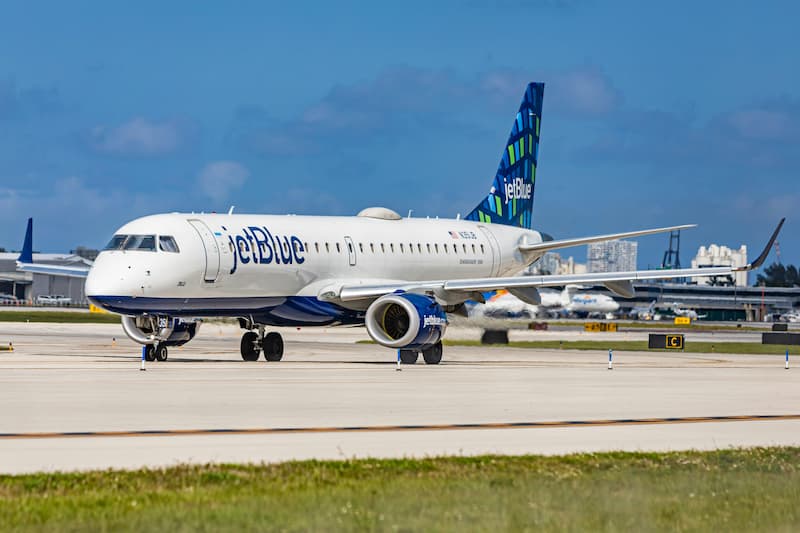 A JetBlue aircraft on an airport tarmac under a sunny sky.