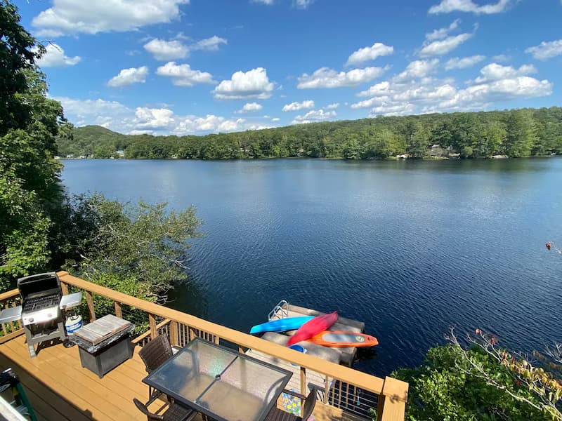 A wooden deck with a grill and outdoor seating overlooking a calm lake