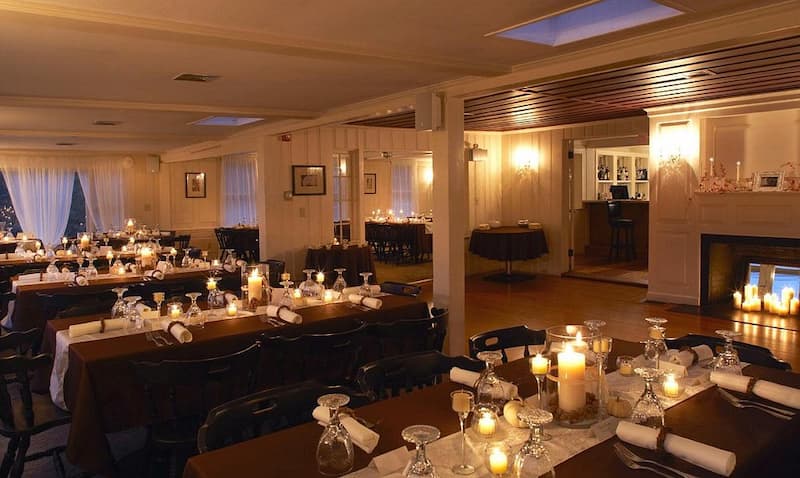 A cozy restaurant dining room warmly illuminated by dozens of candles on tables and a fireplace.