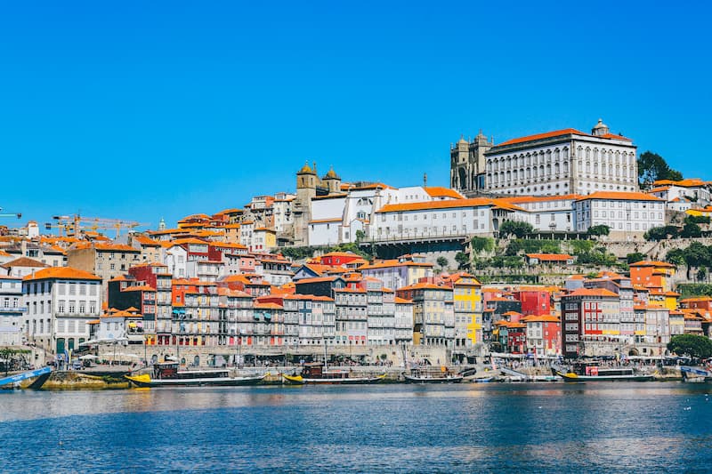 Colorful houses line the Douro River in Porto, Portugal, under a clear blue sky.