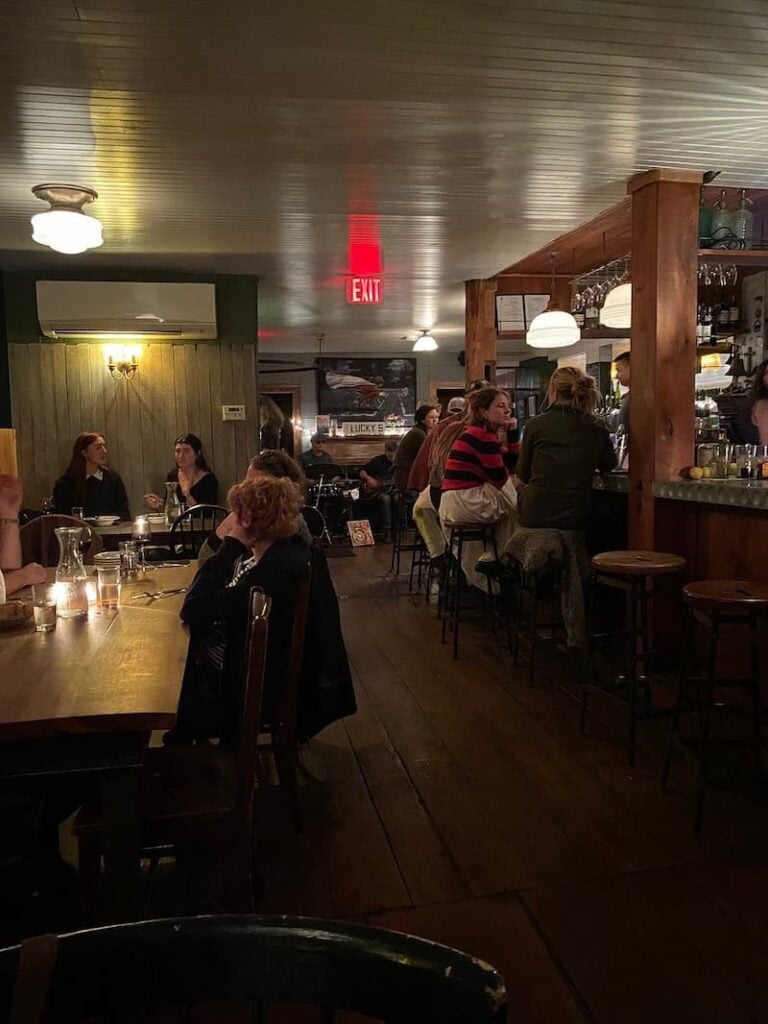 A dim restaurant interior at Prairie Whale with patrons seated at tables and a long bar.