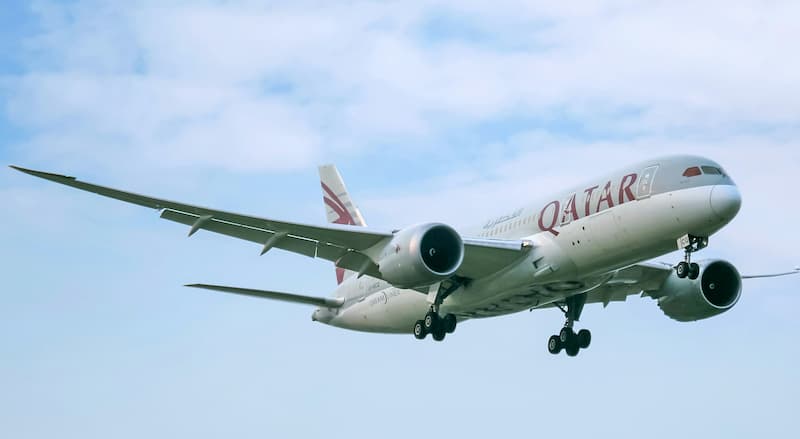 A Qatar Airways plane in flight against a partly cloudy sky.