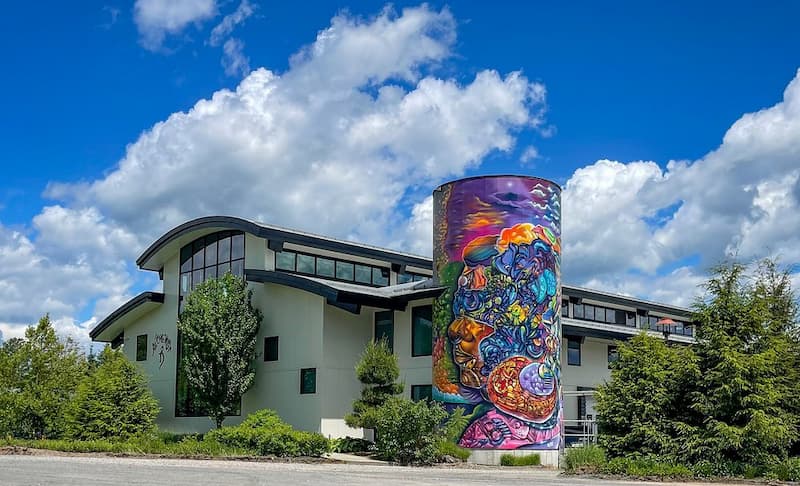 The modern exterior of The Alchemist brewery with its iconic, colorful mural on a silo.