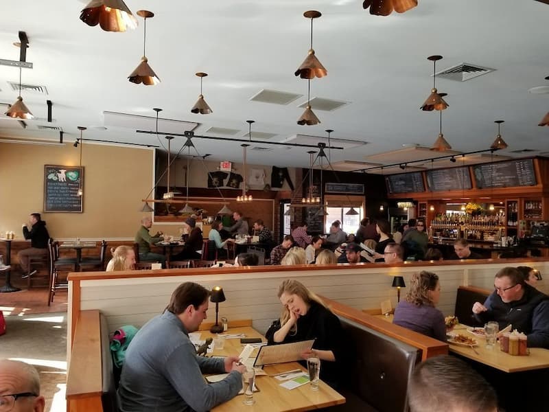 The bustling interior of a tap and grill full of diners sitting in wooden booths.
