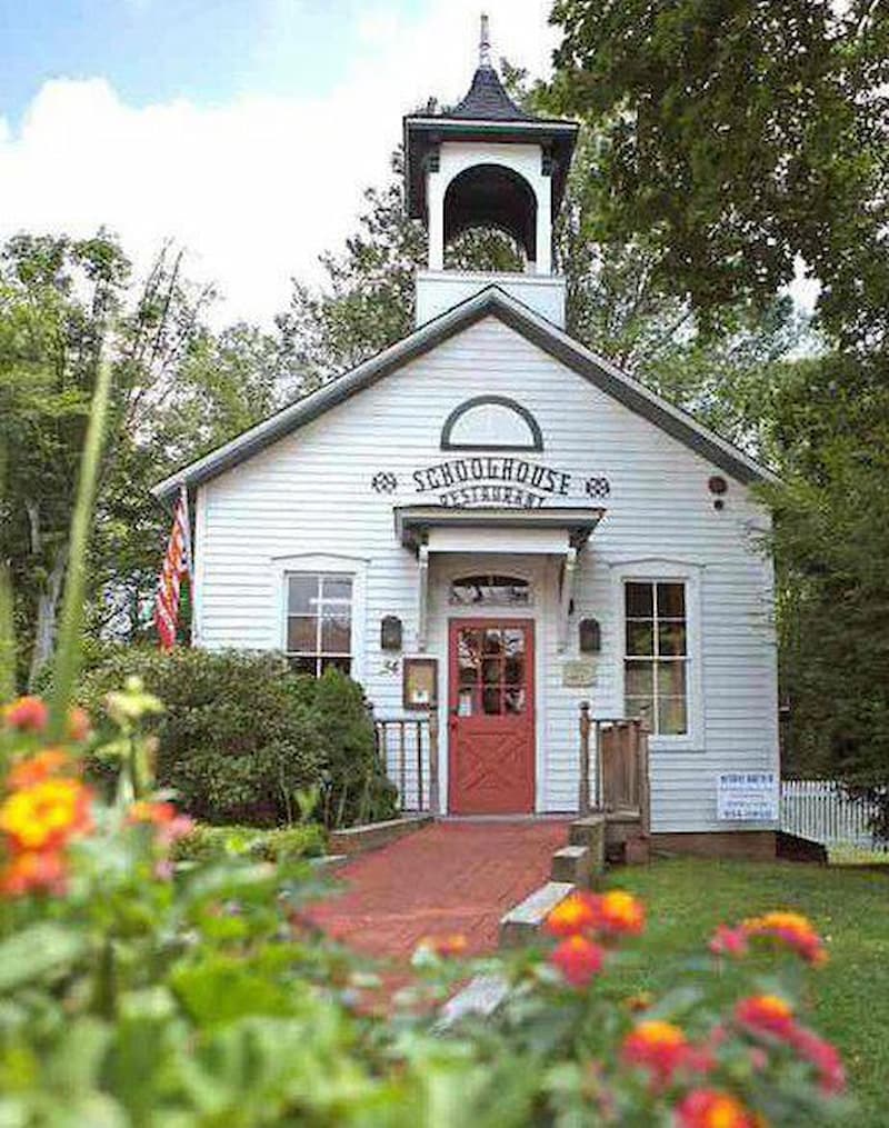 A historic white schoolhouse with a red door and bell tower, now a restaurant.