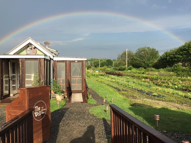 A bright rainbow arches over a small restaurant building next to farm fields.