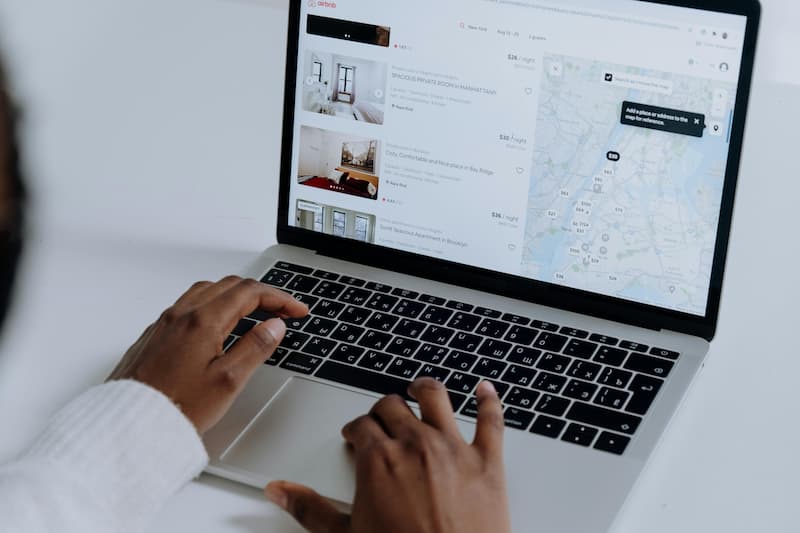 Hands typing on a laptop showing the Airbnb website with search results and a map.