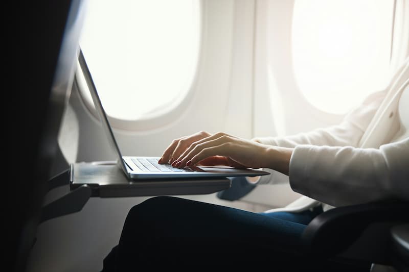 Close-up of hands typing on a laptop keyboard on an airplane's tray table.