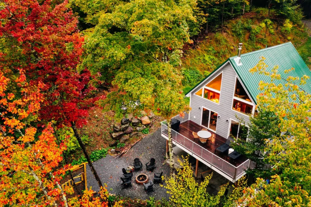 Aerial view of a gray mountain cabin in Vermont with a green metal roof surrounded by vibrant autumn trees
