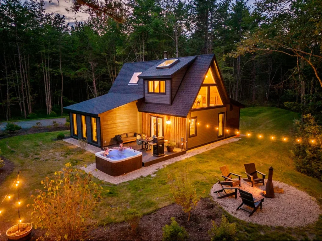 High-angle exterior view of a modern cabin at dusk with an outdoor hot tub and fire pit