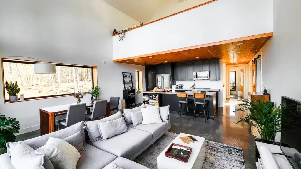 Open-concept cabin living room with a grey sectional, kitchen island, and a loft overhead
