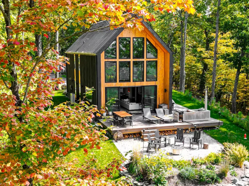 High-angle exterior view of a modern two-story black cabin with a glass facade surrounded by autumn foliage