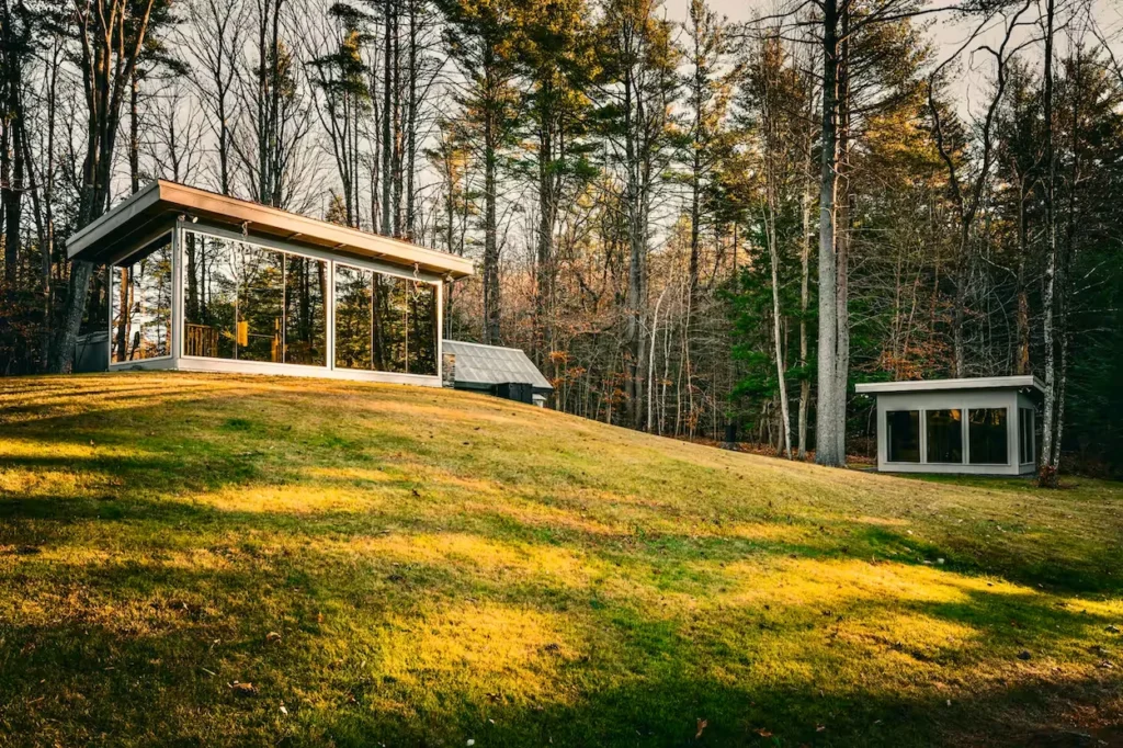 Exterior view of the modern Vermont Mirror House glass pavilions sitting on a grassy hill surrounded by trees