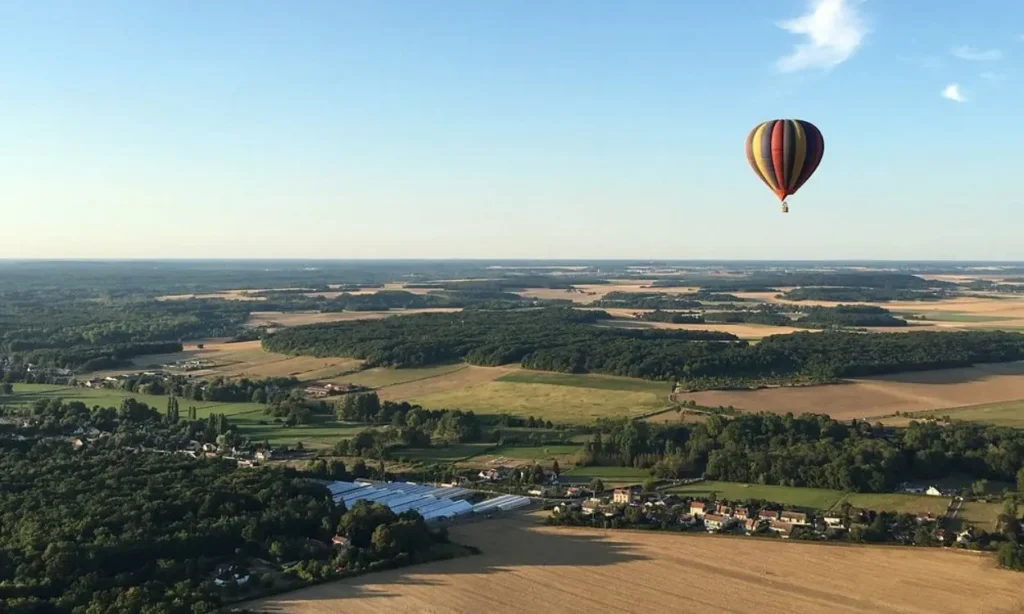 A colorful hot air balloon floating above fields and forests near Fontainebleau.