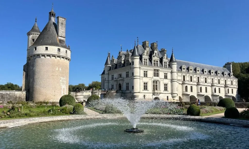 A grand Loire Valley castle with a fountain in the foreground under a clear blue sky.