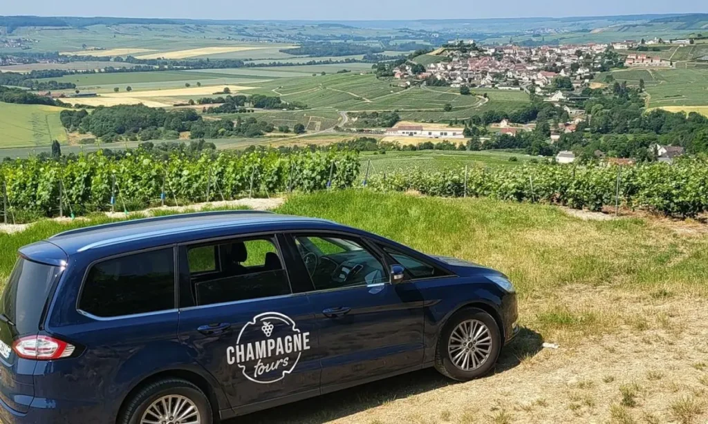 A Champagne Tours car parked by scenic vineyards overlooking a village.