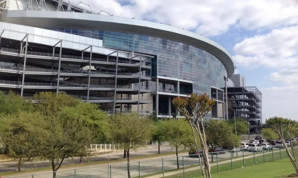Exterior view of NRG Stadium with trees and cars in the foreground.