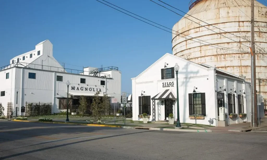 White buildings and a large silo at Magnolia Silos on a clear day.