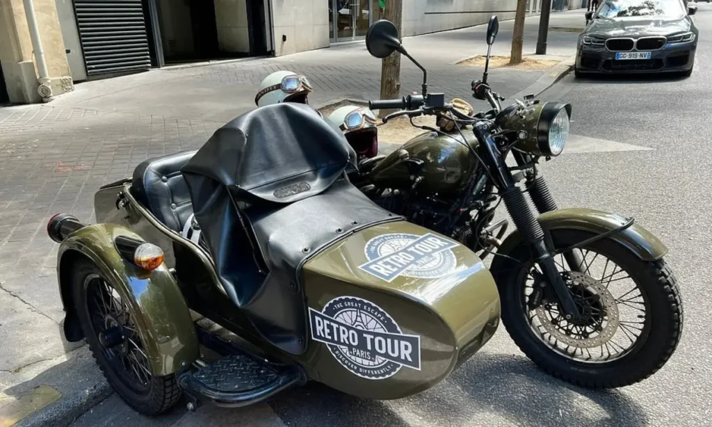 A retro green motorcycle with a sidecar parked on a Paris street.