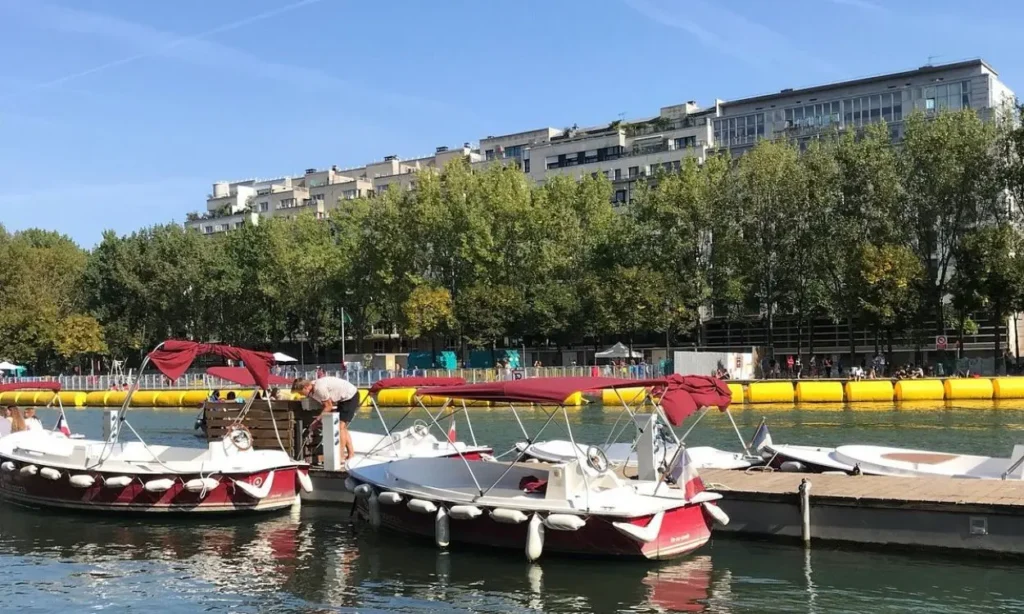 Red and white boats with canopies moored at a dock on a sunny day at Marin D’Eau Douce in Paris.