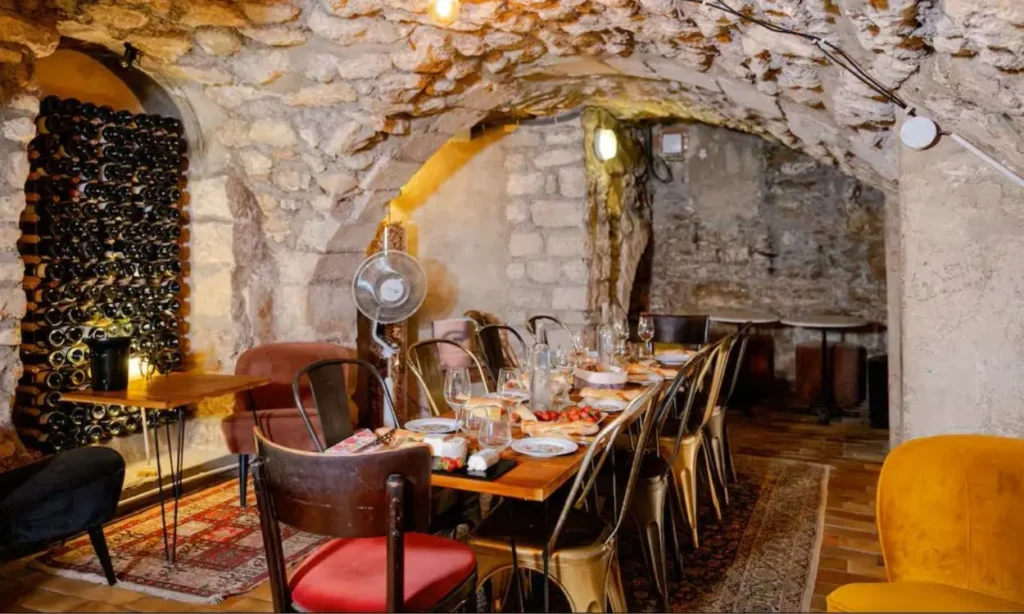 A long wooden table set for dinner inside a rustic stone-walled wine cellar in Paris.