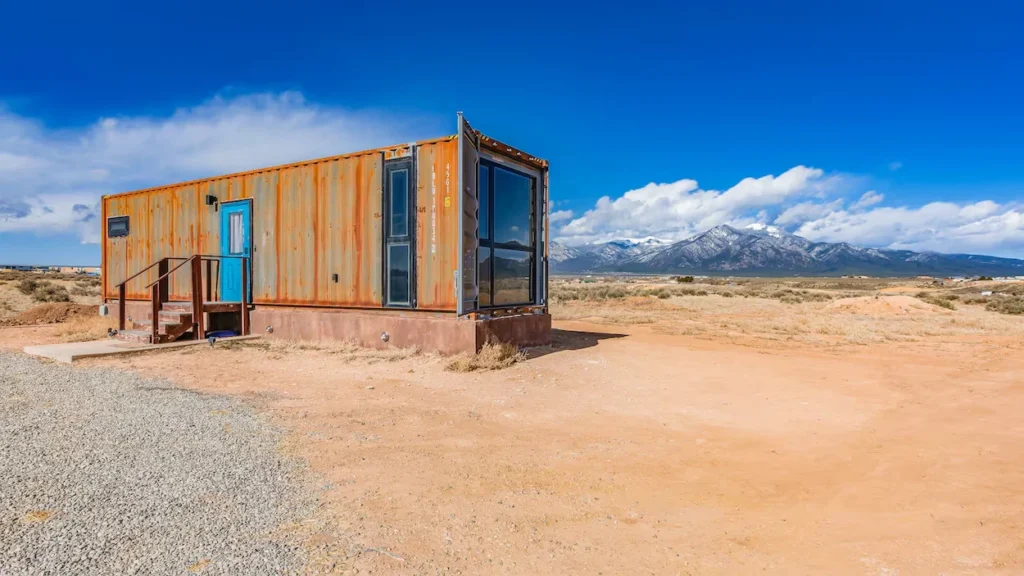 Rusted shipping container home on a desert plot with mountains in the background