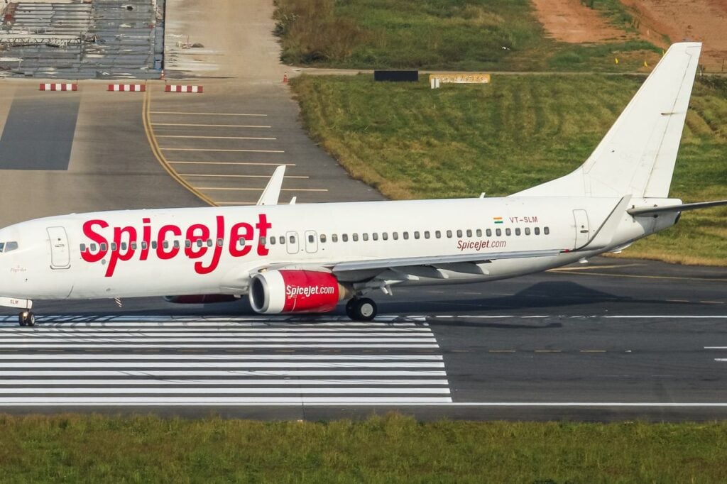 A white SpiceJet passenger airplane taxiing past a marked runway threshold