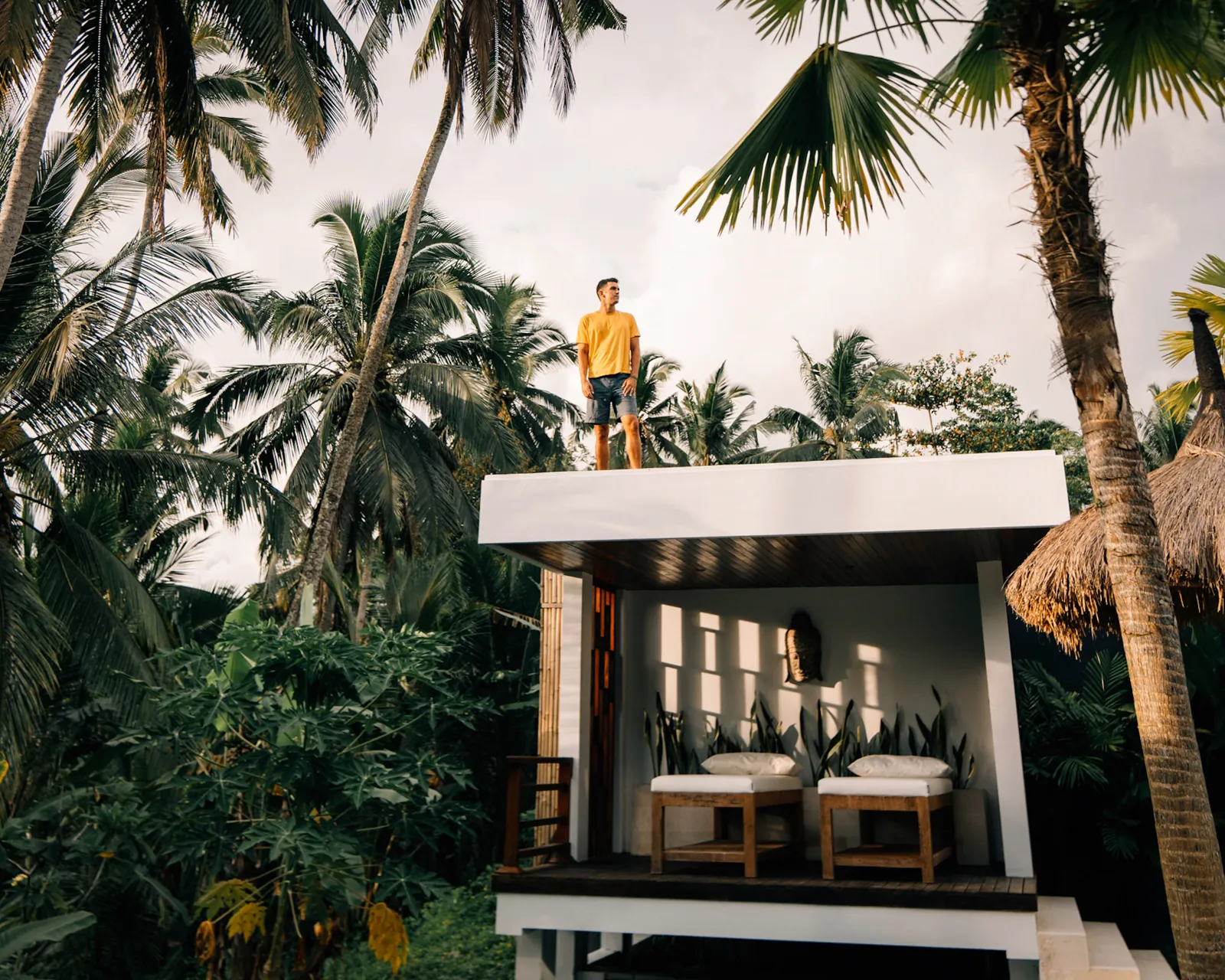 Jon Miksis in a yellow shirt standing above an open-air pavilion surrounded by palm trees in Bali.